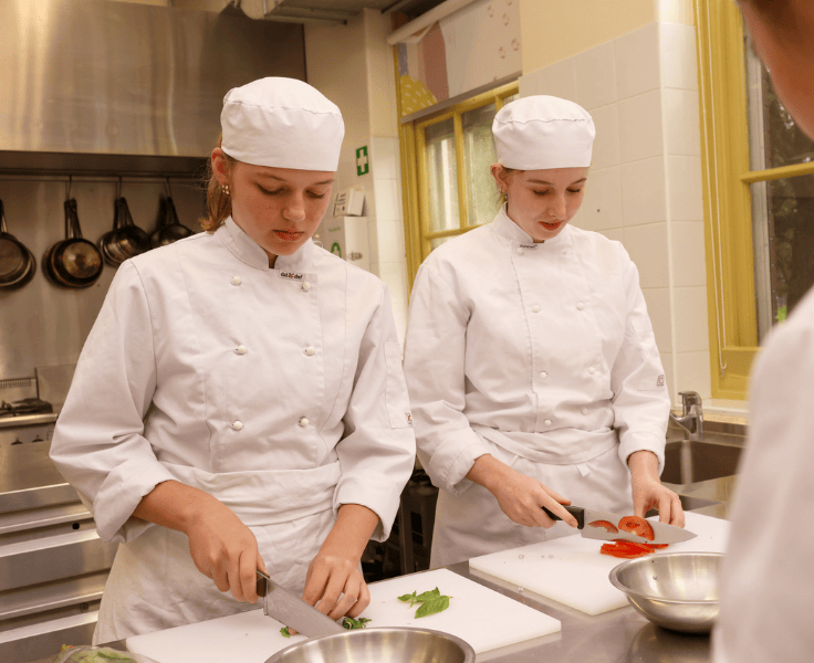 two students chopping vegetables in a kitchen