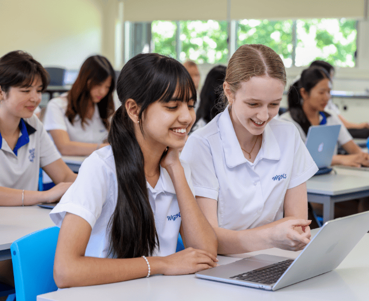 Students sitting in a bright classroom looking at a laptop computer